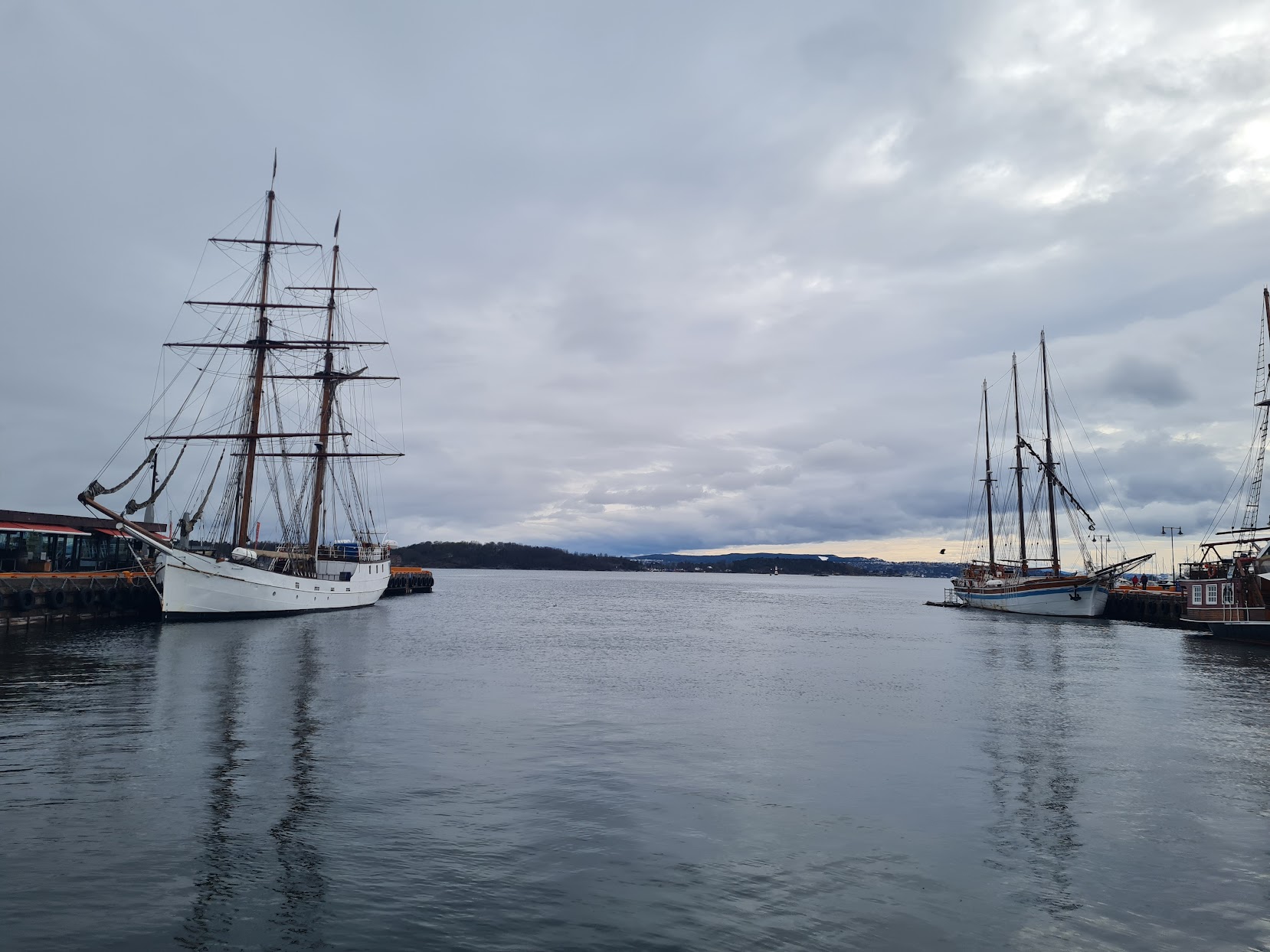 Photo of Oslo's Fjord on a cloudy day showing two tall ships with rigging.